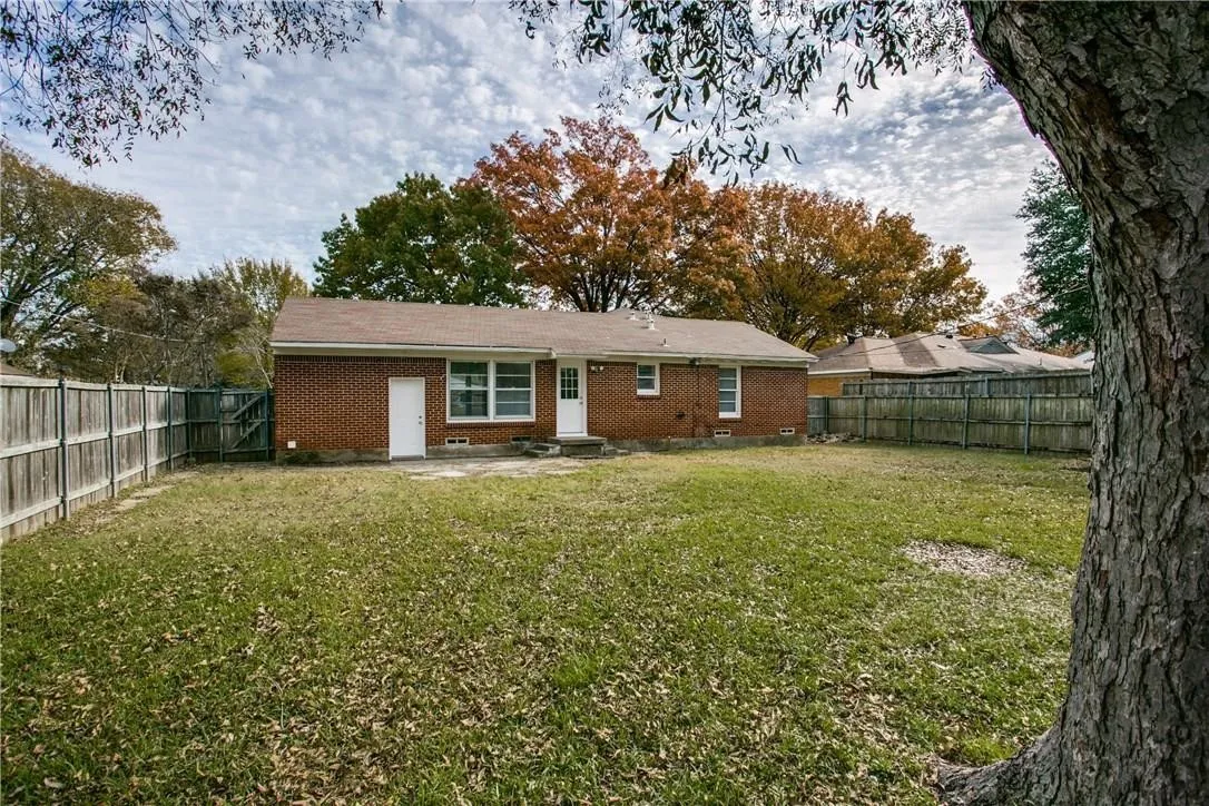 Brick exterior with a brown shingle roof, accompanied by a wooden privacy fence, and a spacious green lawn
