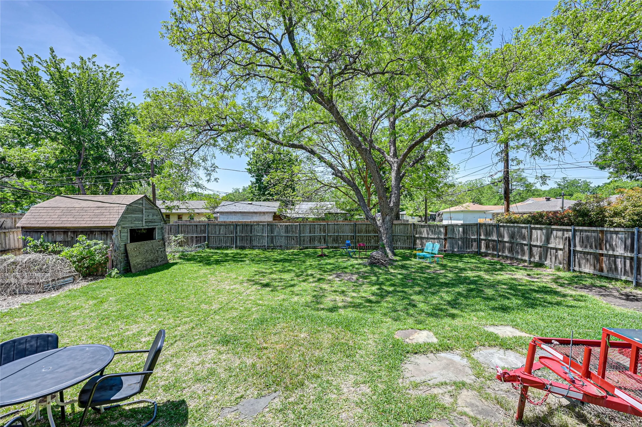 Expansive backyard featuring a large mature tree, wood privacy fencing, and a storage shed