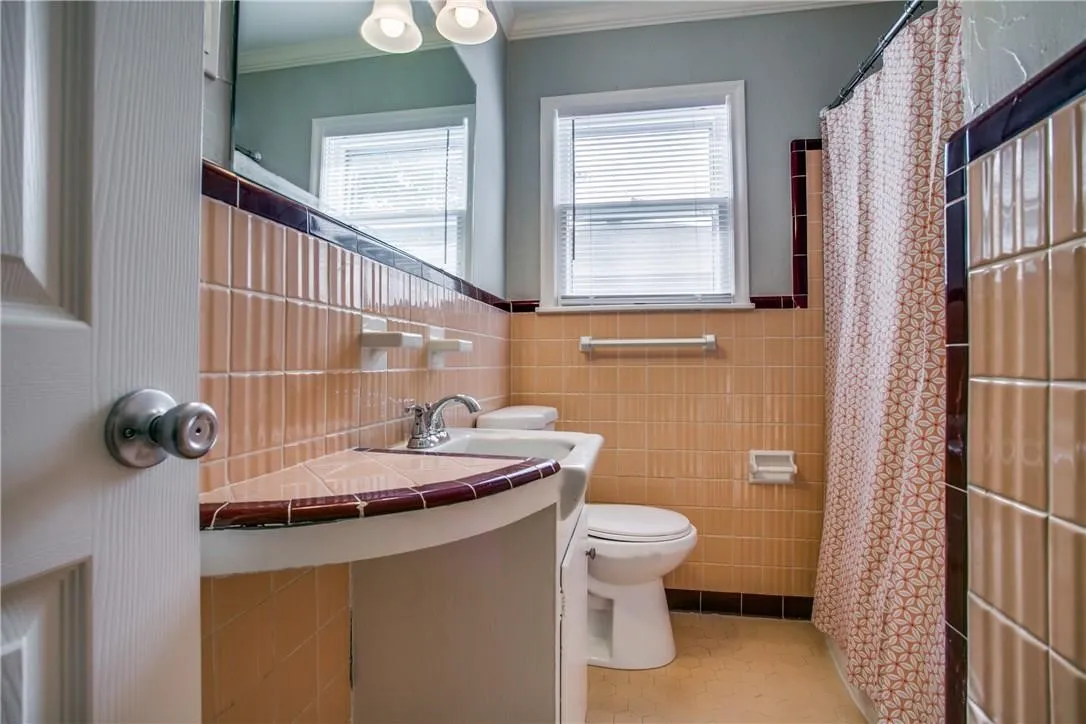 Pedestal sink with tiled counter, full tiled walls, and a window with blinds