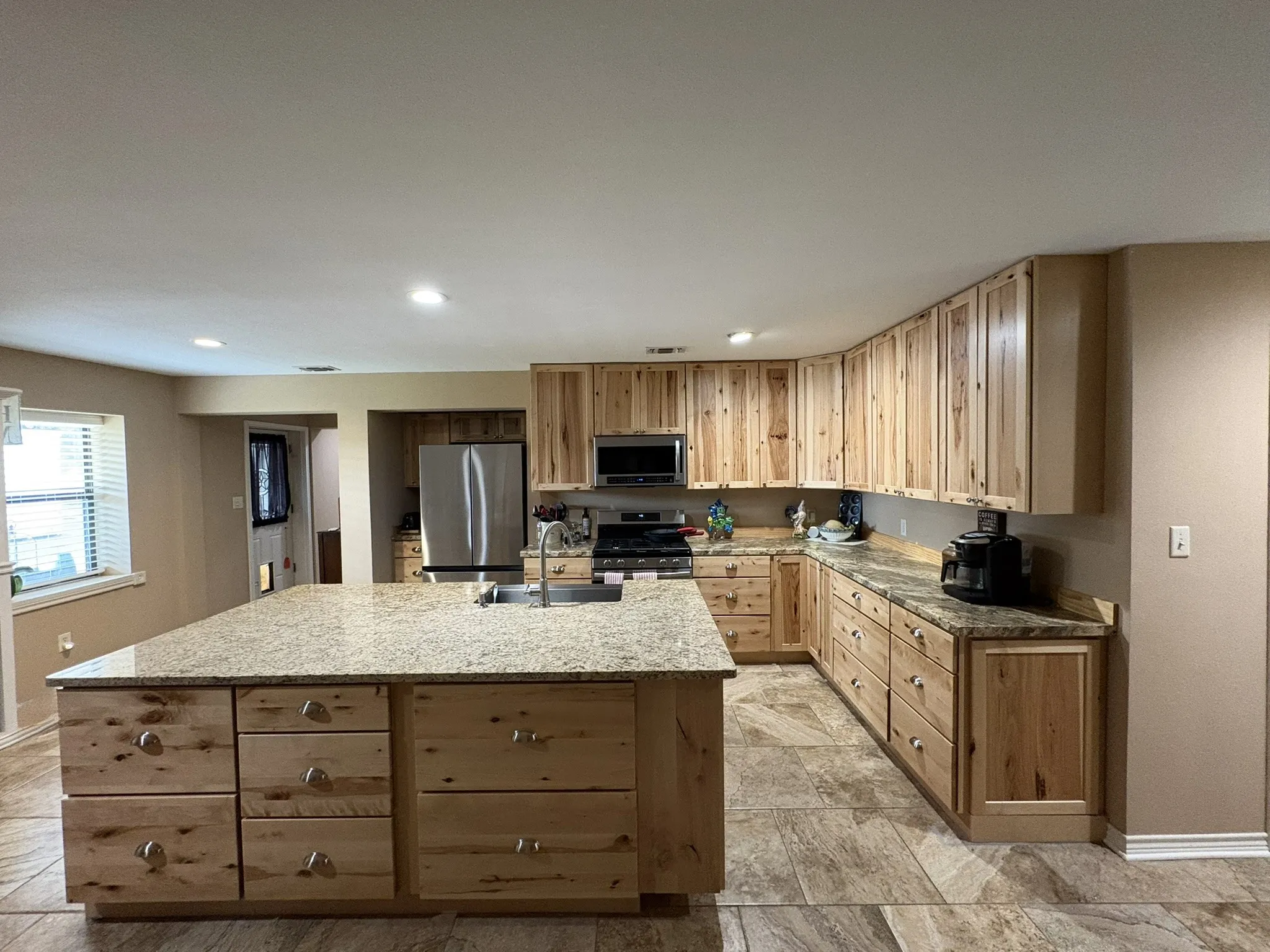 Spacious kitchen with a central island, light-toned wood cabinetry, granite-finish countertops, stainless steel appliances, and tile flooring