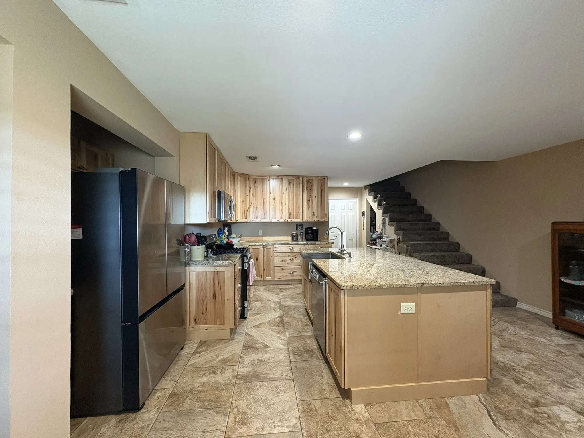 Kitchen featuring wood-finish cabinetry, stainless steel appliances, a large center island with a sink, and stone-finish flooring