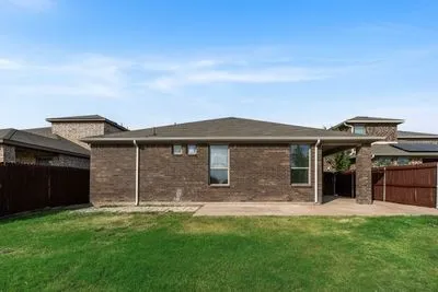 Brick exterior with covered patio, wood fencing, and a grassy outdoor area