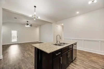 Kitchen island with a double basin sink and granite-finish countertop, wood-finish flooring, recessed lighting, and wainscoting