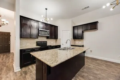 Kitchen featuring dark wood-finish cabinetry, granite countertops, stainless steel microwave, black electric range, and wood-finish flooring