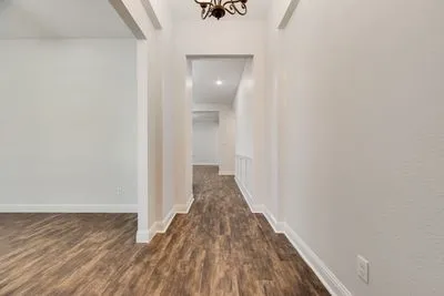 Wood-finish flooring throughout, white wall finishes, crown molding, and an overhead chandelier