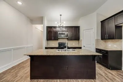 Kitchen featuring a large central island with an undermount sink, dark wood-finish cabinetry, light-toned backsplash, and recessed lighting