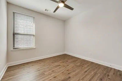 Wood-finish flooring, white walls, window with blinds, and ceiling fan with integrated lighting