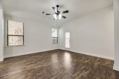 Vaulted ceiling, two windows with blinds, wood-finish flooring, ceiling fan with integrated lighting, and a glass-paneled door
