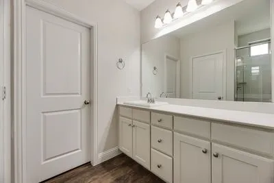 White vanity with integrated sink, expansive mirror, four-light vanity fixture, and wood-finish flooring
