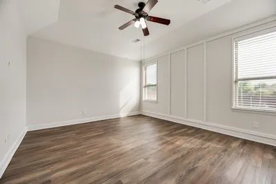 Wood-finish flooring, vaulted ceiling, ceiling fan, two windows with blinds, and decorative wall paneling