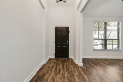 Entryway featuring a dark wood-finish door, wood-finish flooring, white walls, and a large window with blinds