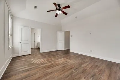 Wood-finish flooring, vaulted ceiling, ceiling fan with light fixture, white interior doors, and window with blinds