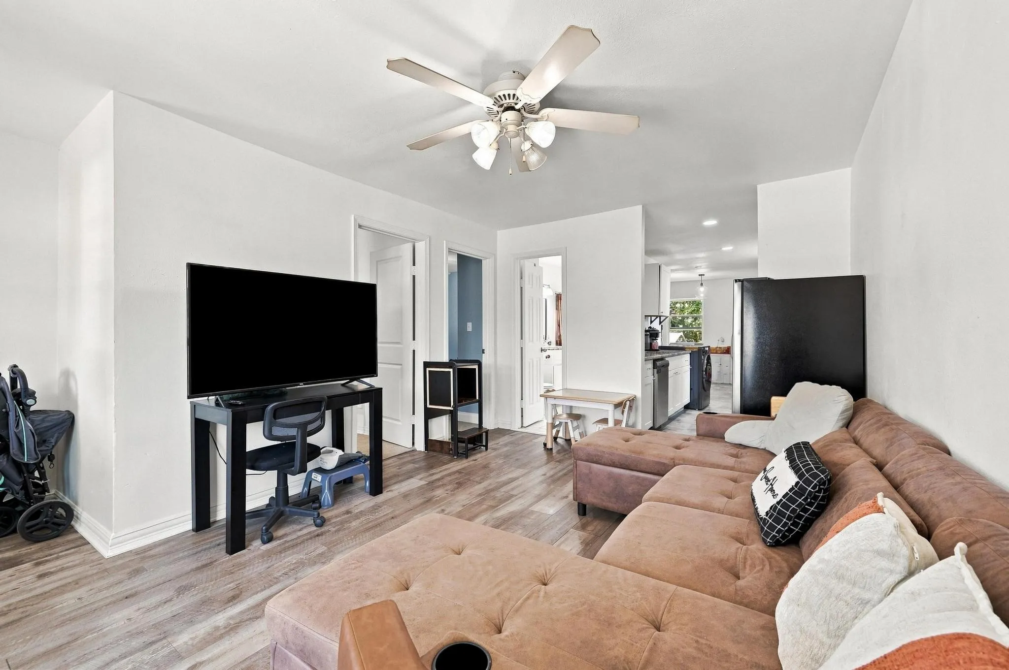 Open-concept living area with wood-finish flooring, white walls, and a ceiling fan with integrated lighting