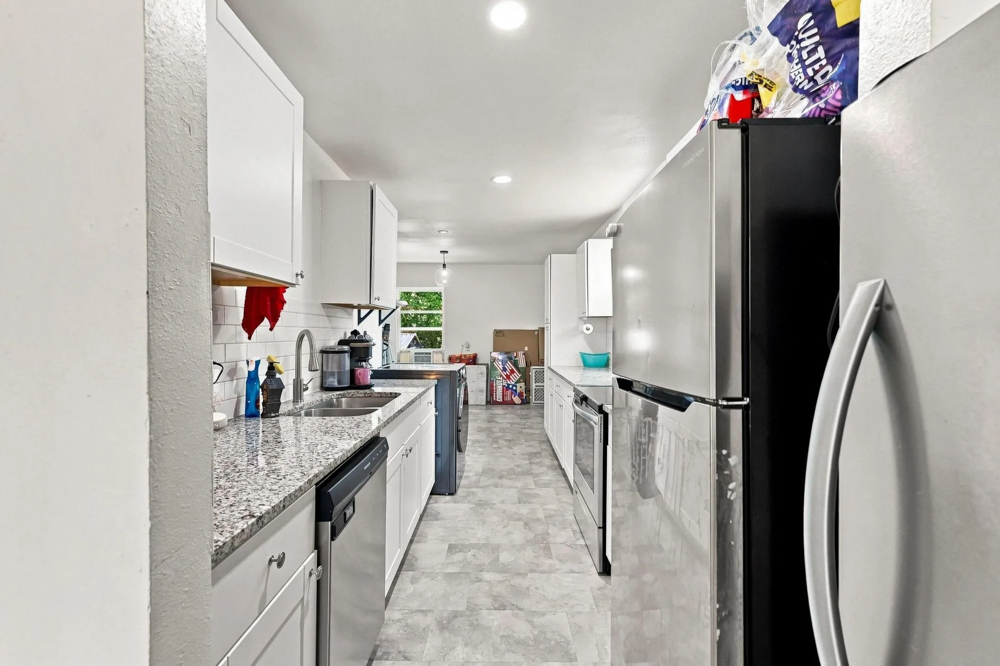 Galley kitchen featuring white cabinetry, granite-style countertops, stainless steel appliances including a refrigerator and dishwasher, tile flooring, and recessed lighting throughout