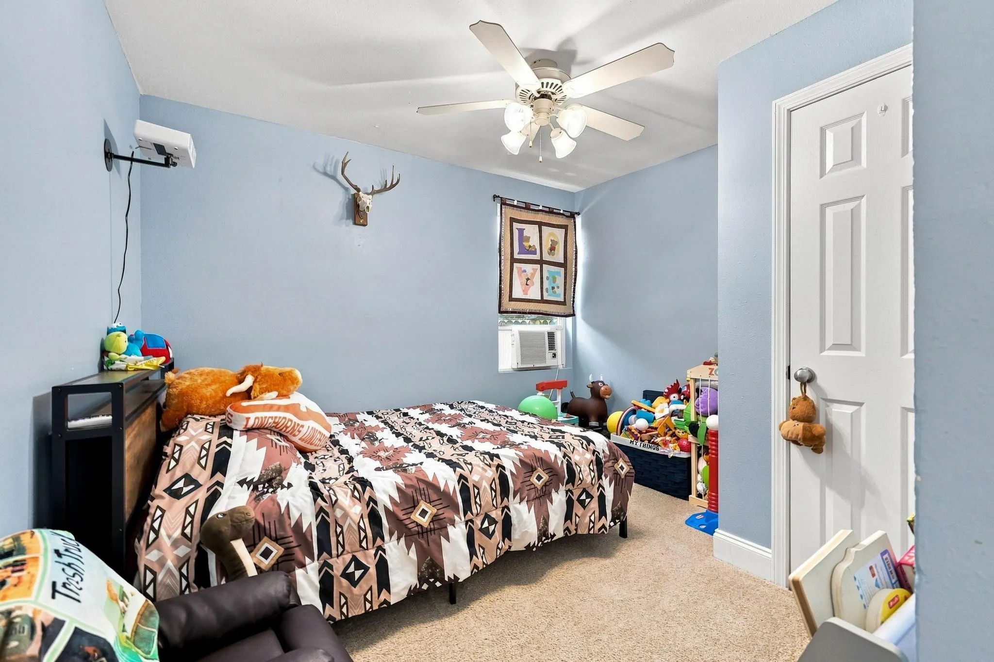 Spacious bedroom with light blue walls, ceiling fan with integrated lighting, and neutral carpeting