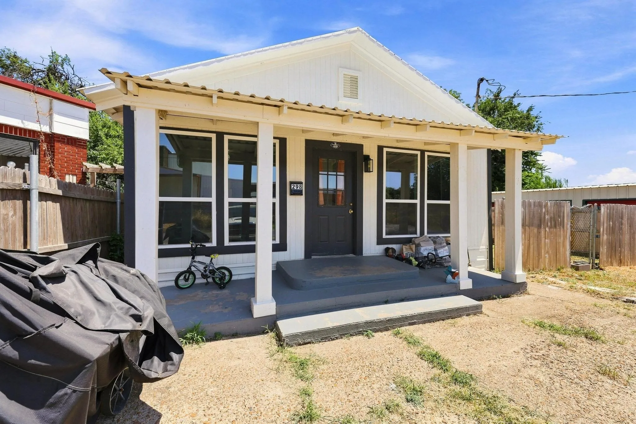 Modern cottage-style home featuring a spacious covered front porch with composite decking, large multi-pane windows and glass doors, clean white exterior with contrasting trim, and a gabled roofline