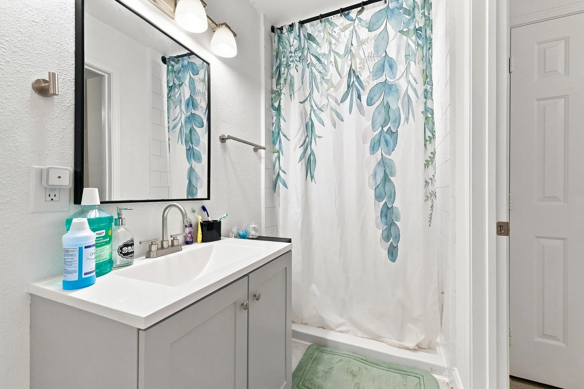 Vanity with a white countertop and undermount sink, brushed nickel faucet, large framed mirror, and two-light fixture