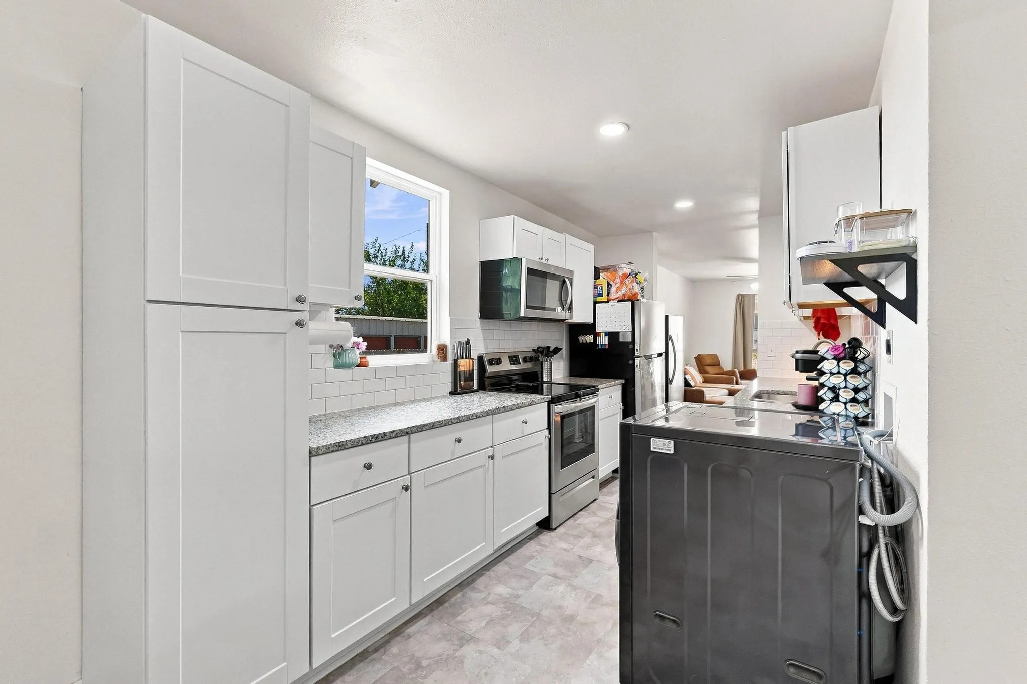 White shaker-style cabinetry with dark hardware, speckled countertops, subway tile backsplash, and recessed lighting