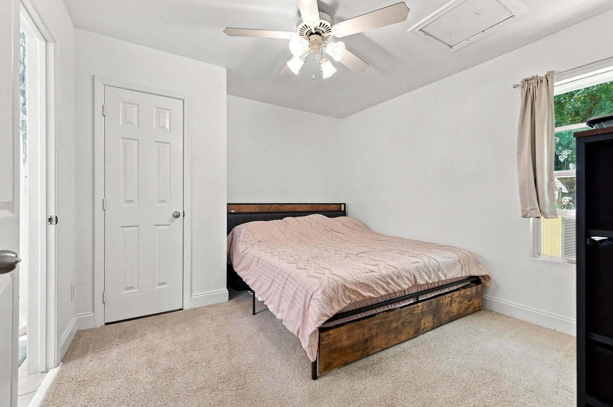 Ceiling fan fixture, white paneled door, light-toned carpeting, window with outdoor scenery, attic access panel