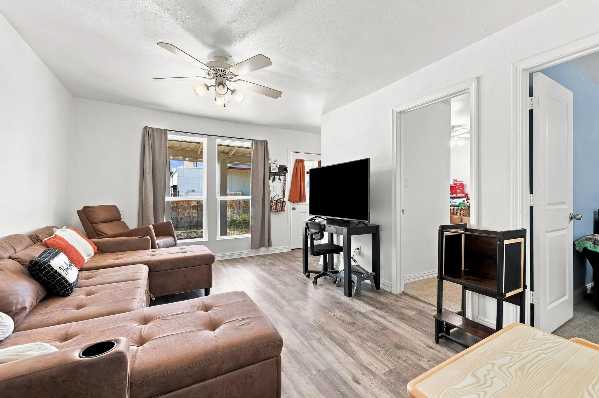 Bright, open-concept living area showcasing wood-finish flooring throughout, ceiling fan with integrated lighting, and sliding glass doors with natural light
