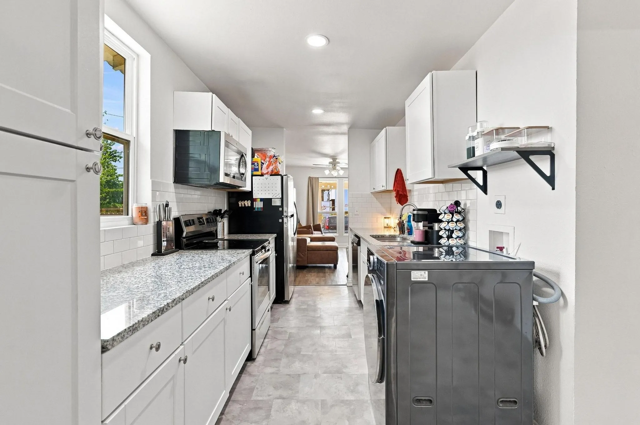 Galley kitchen featuring white cabinetry, gray-finish flooring, stainless steel appliances, and light-filled layout with recessed ceiling lighting