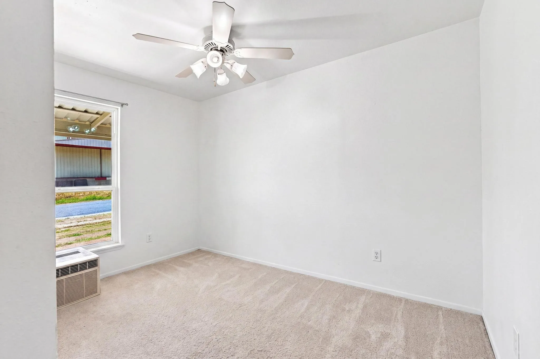 Bright, neutral bedroom featuring neutral carpet flooring, a ceiling fan with integrated lighting, and large window with natural light