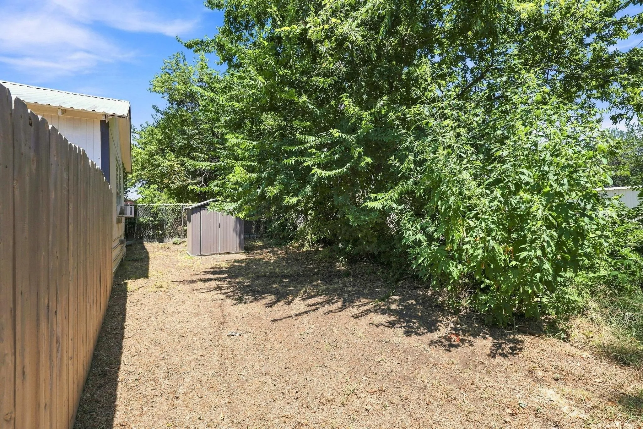 Private backyard featuring a wood privacy fence, mature trees, and an auxiliary storage shed