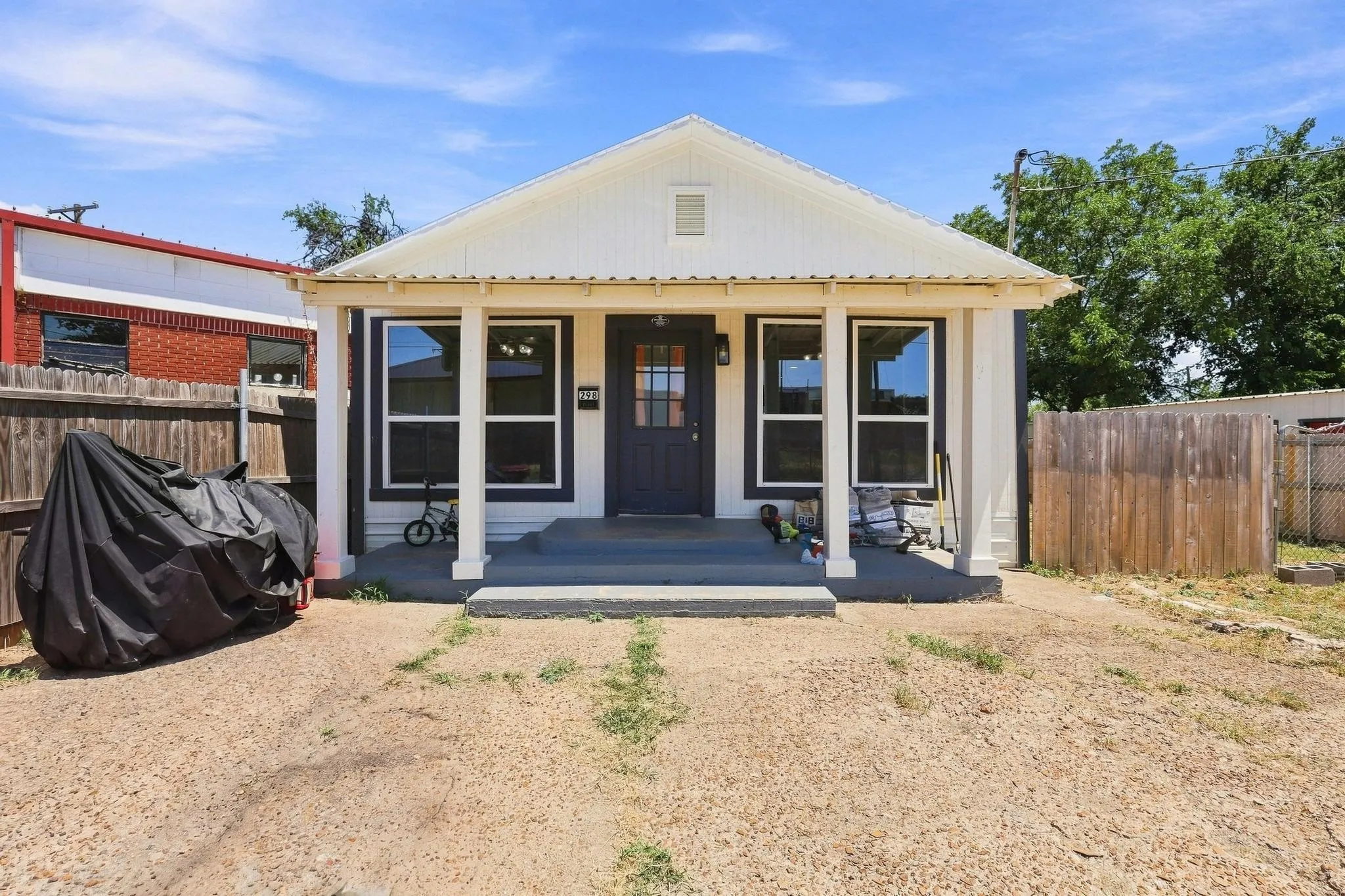 Charming single-story residence featuring a welcoming front porch with black-framed French doors and matching sidelights, gabled roofline with cream exterior, and expansive windows flooding the home with natural light