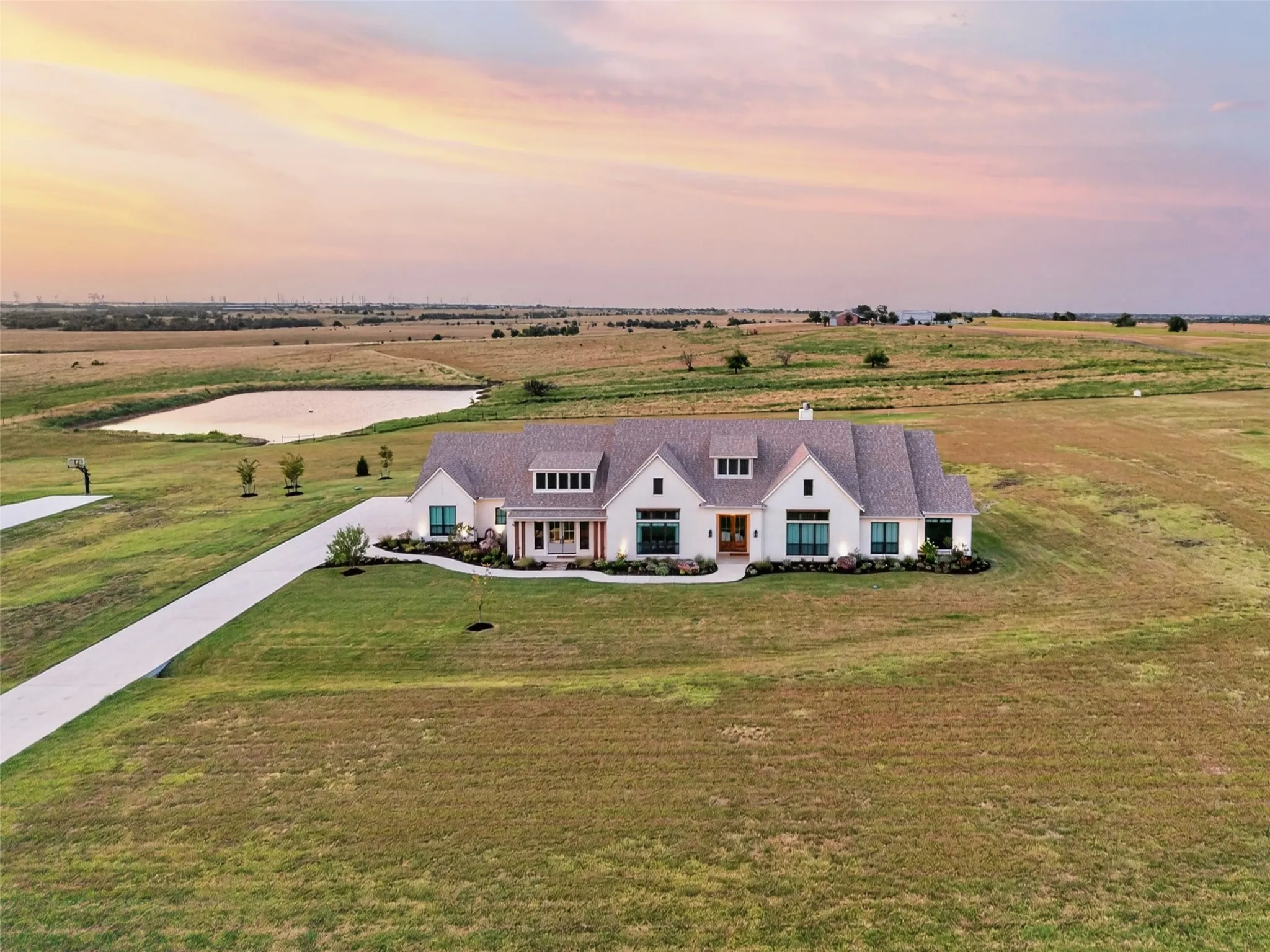 Expansive property featuring a white exterior residence, a long paved driveway, a large pond, and a vast surrounding landscape