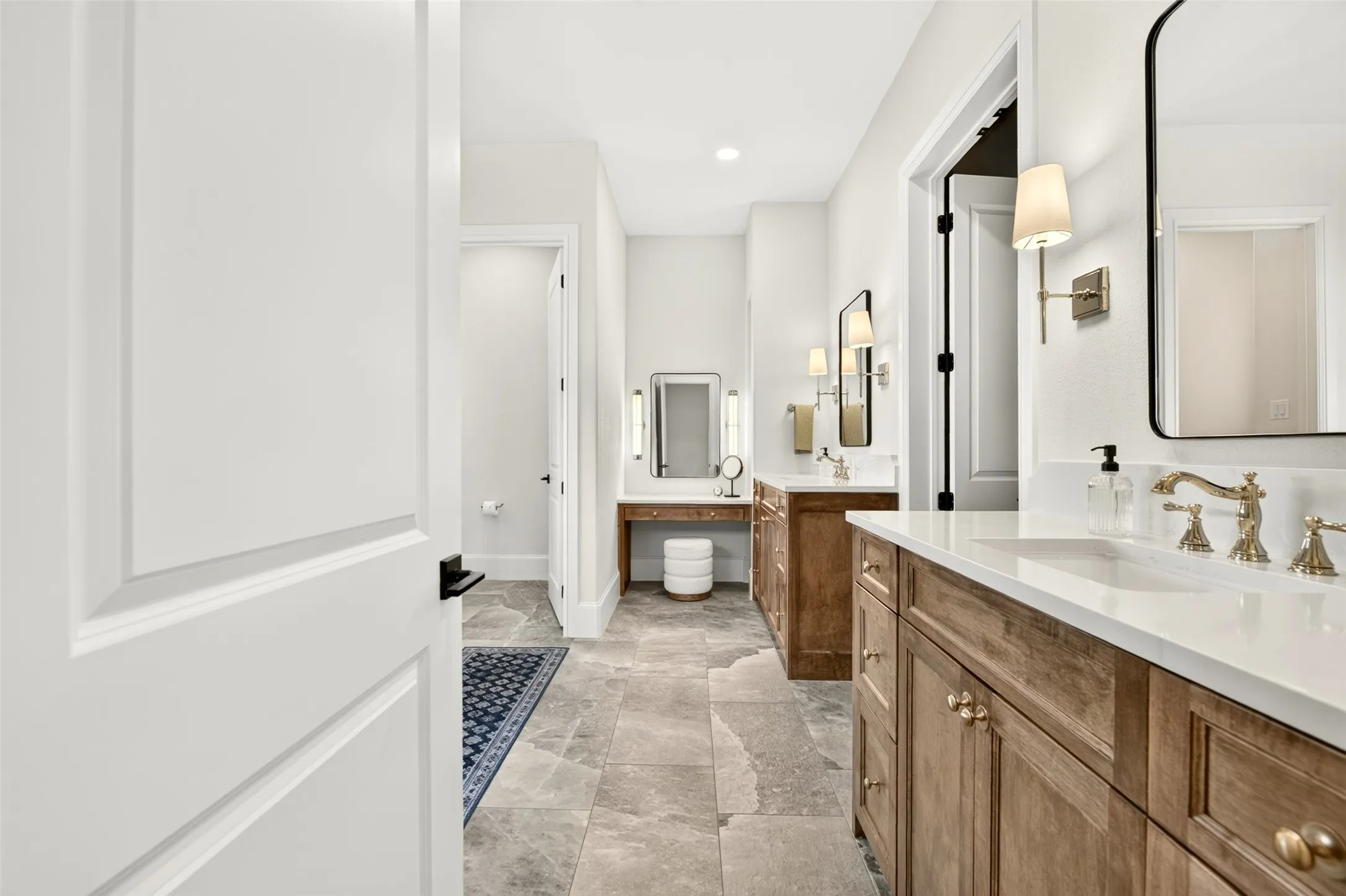 Dual wood-finish vanities with white countertops and undermount sinks, bronze hardware, wall-mounted sconces, and a dedicated vanity desk