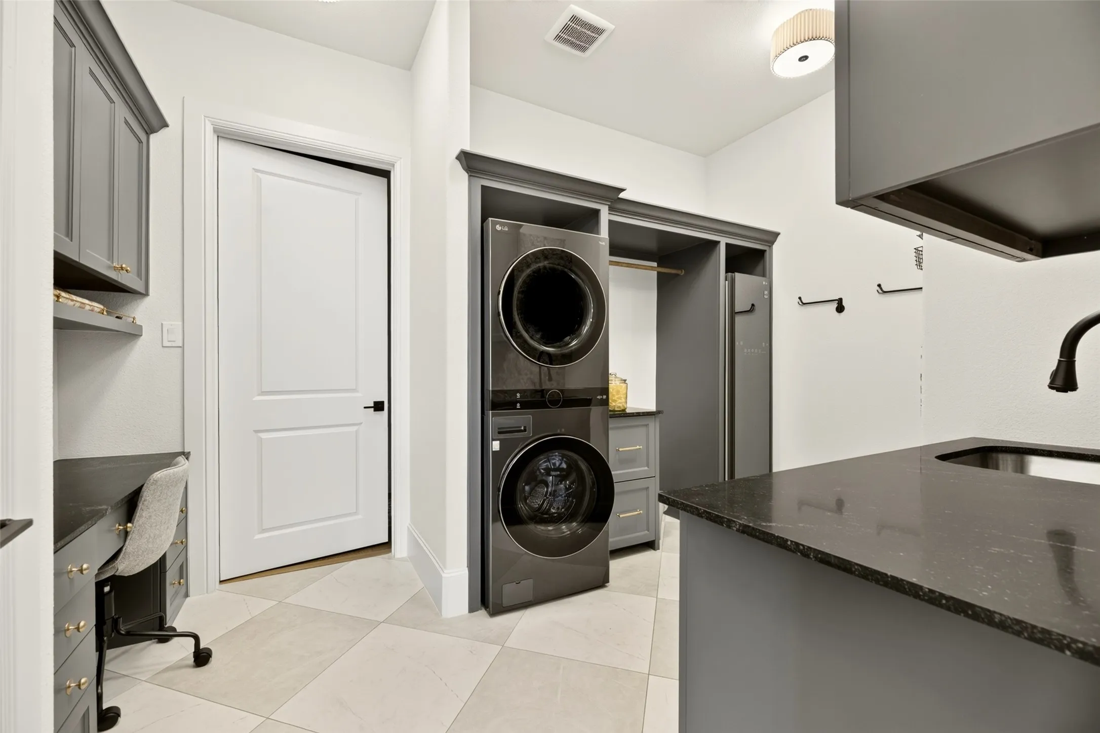 Built-in cabinetry, dark stone countertop, undermount sink, built-in desk, and diamond-patterned floor tiles