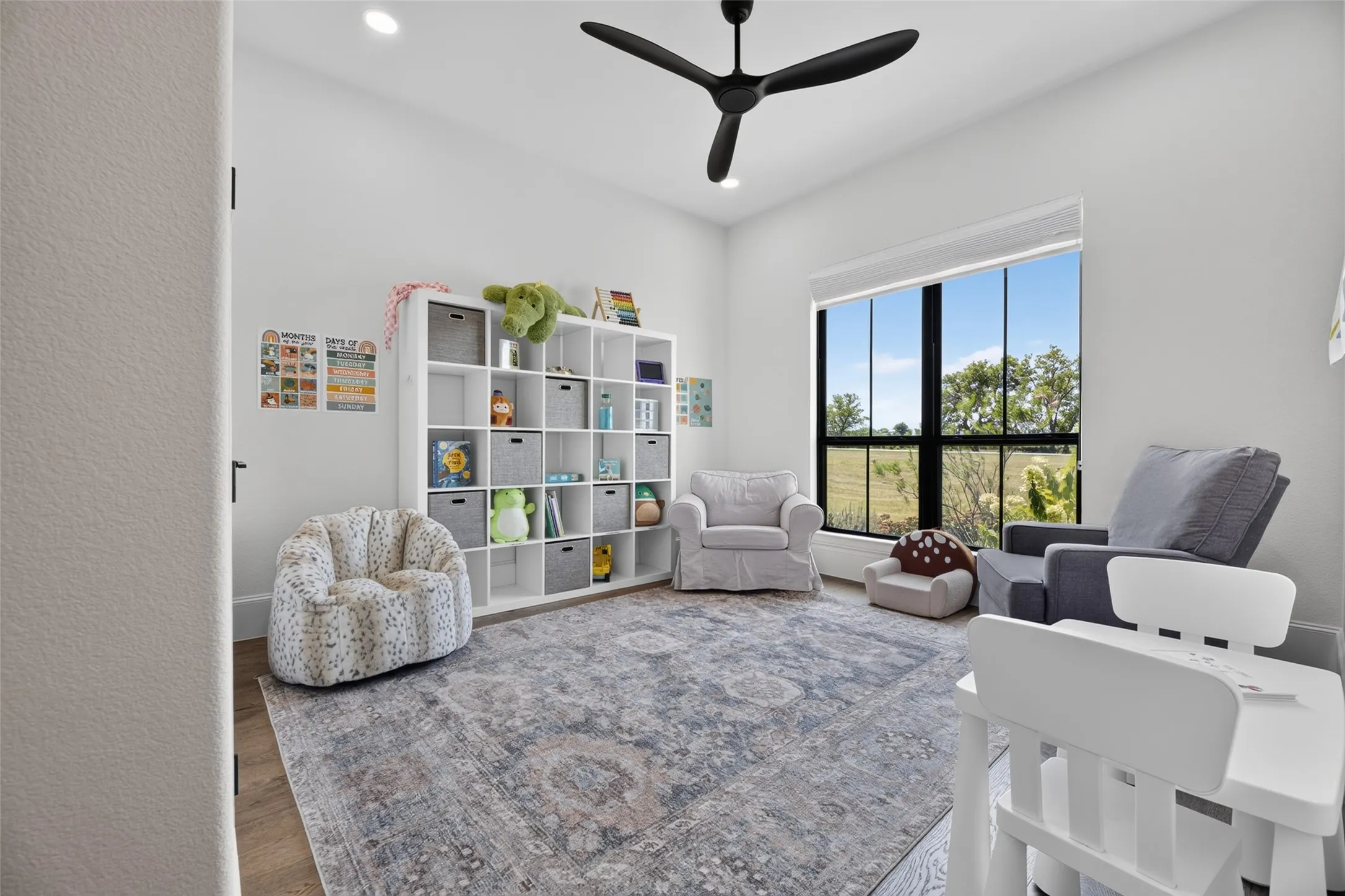 Recessed lighting, wood-finish flooring, a large window with black framing, and a ceiling fan with black blades