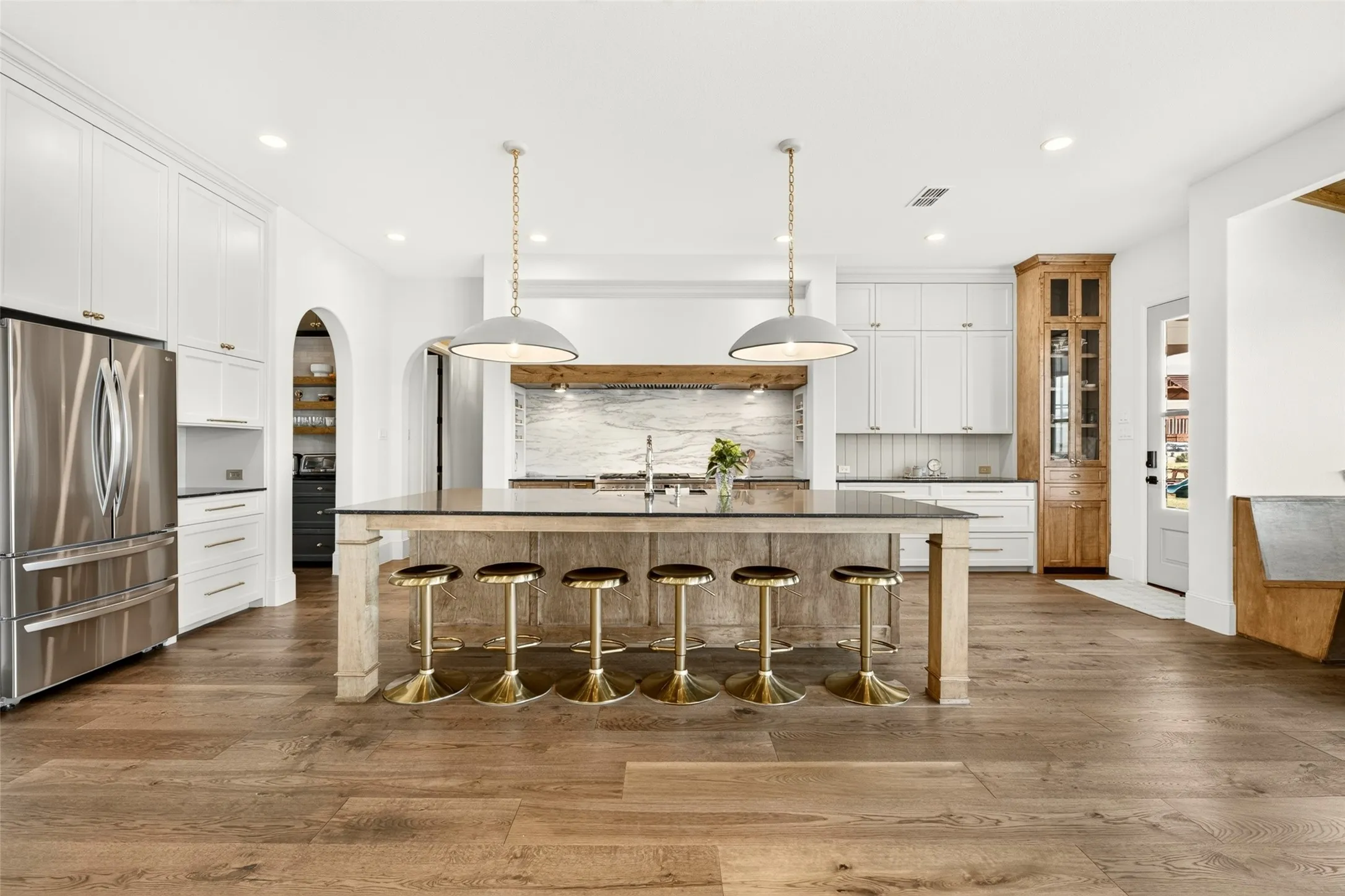 Spacious kitchen featuring wood-finish flooring, white cabinetry, a large kitchen island with a dark countertop, and stainless steel appliances