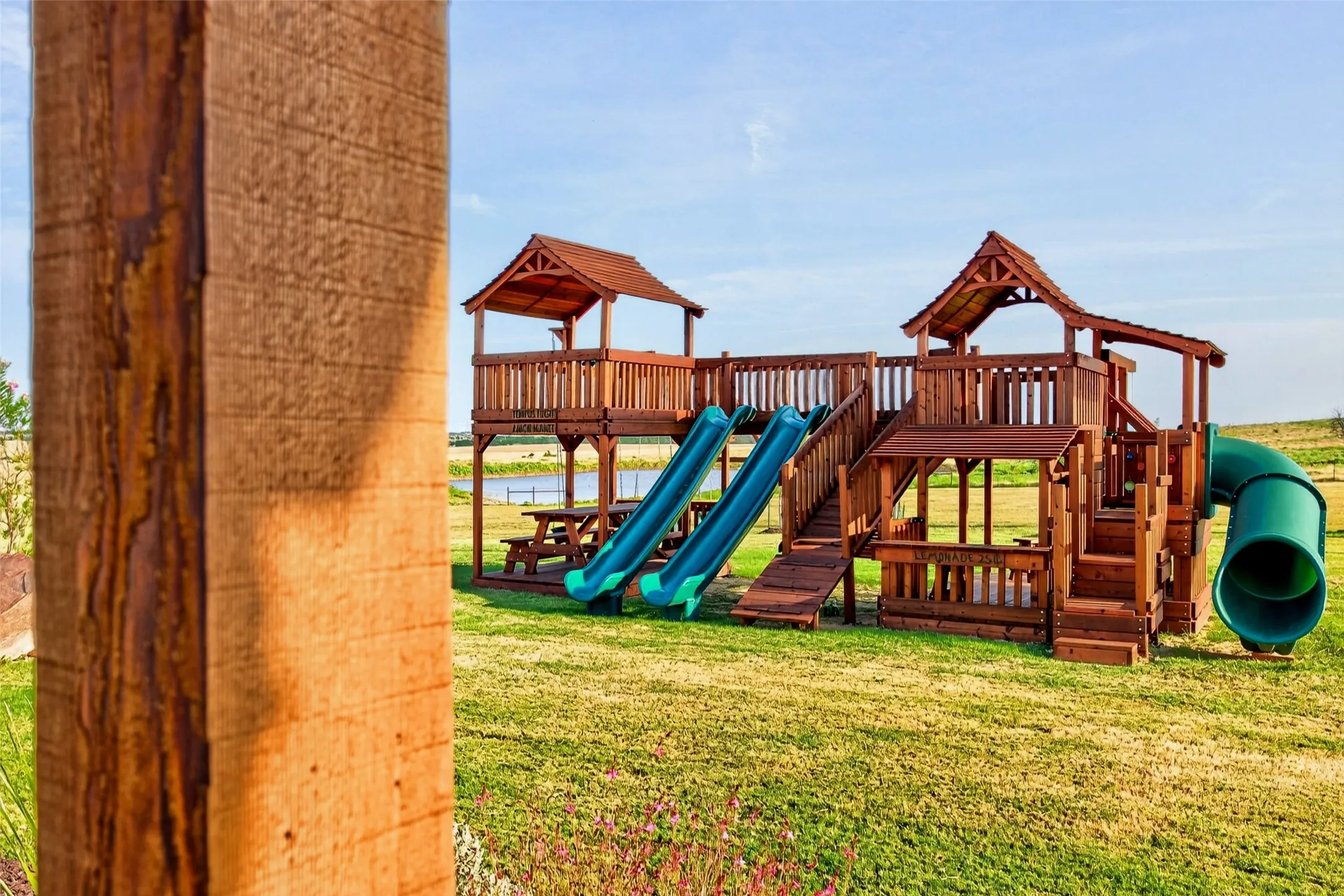 Expansive backyard featuring a multi-level wooden playset with two slides, a tube slide, and a built-in picnic table