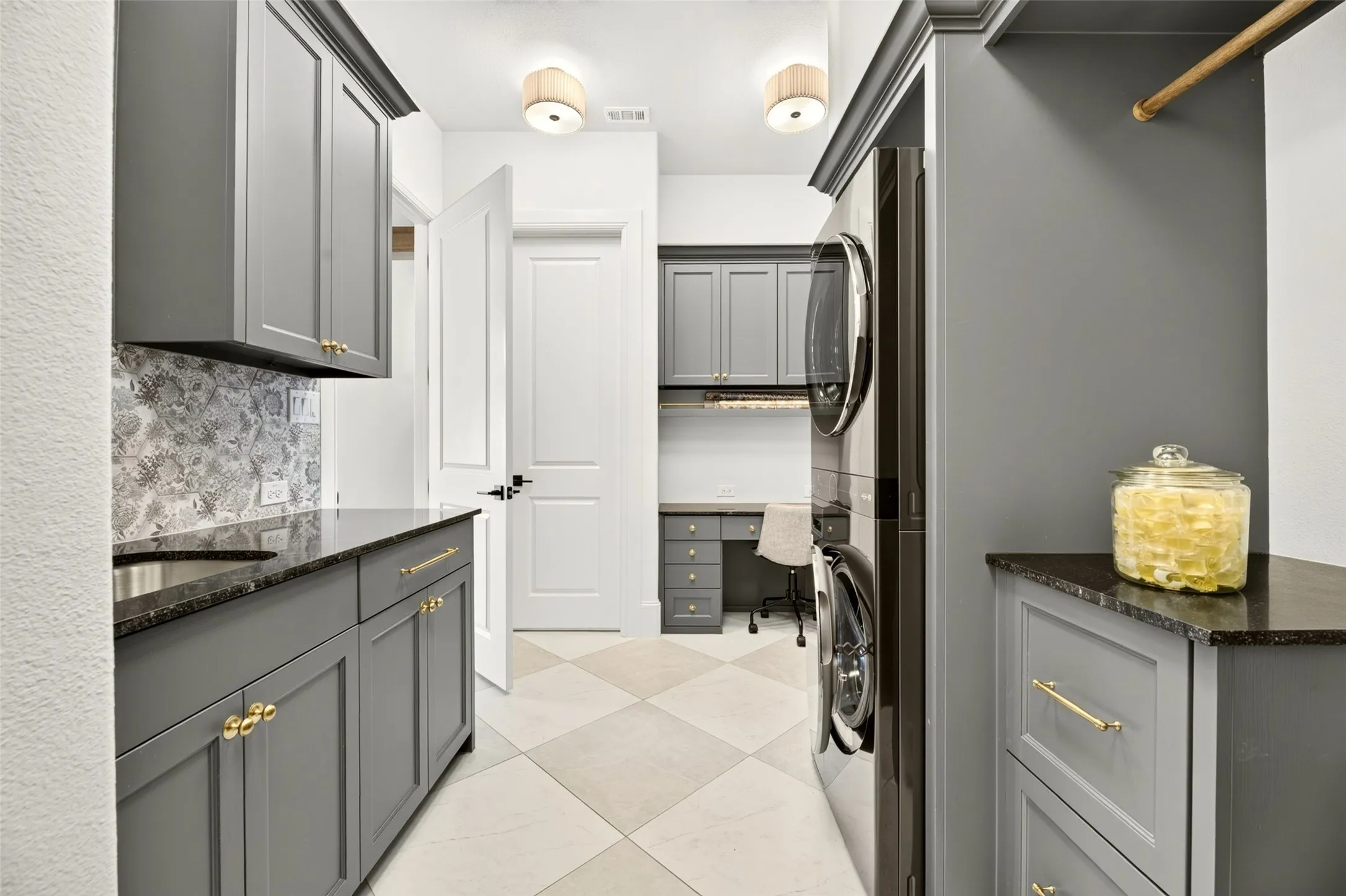 Custom cabinetry with gold-tone hardware, dark countertop, tile backsplash, built-in desk, and checkerboard floor tiles