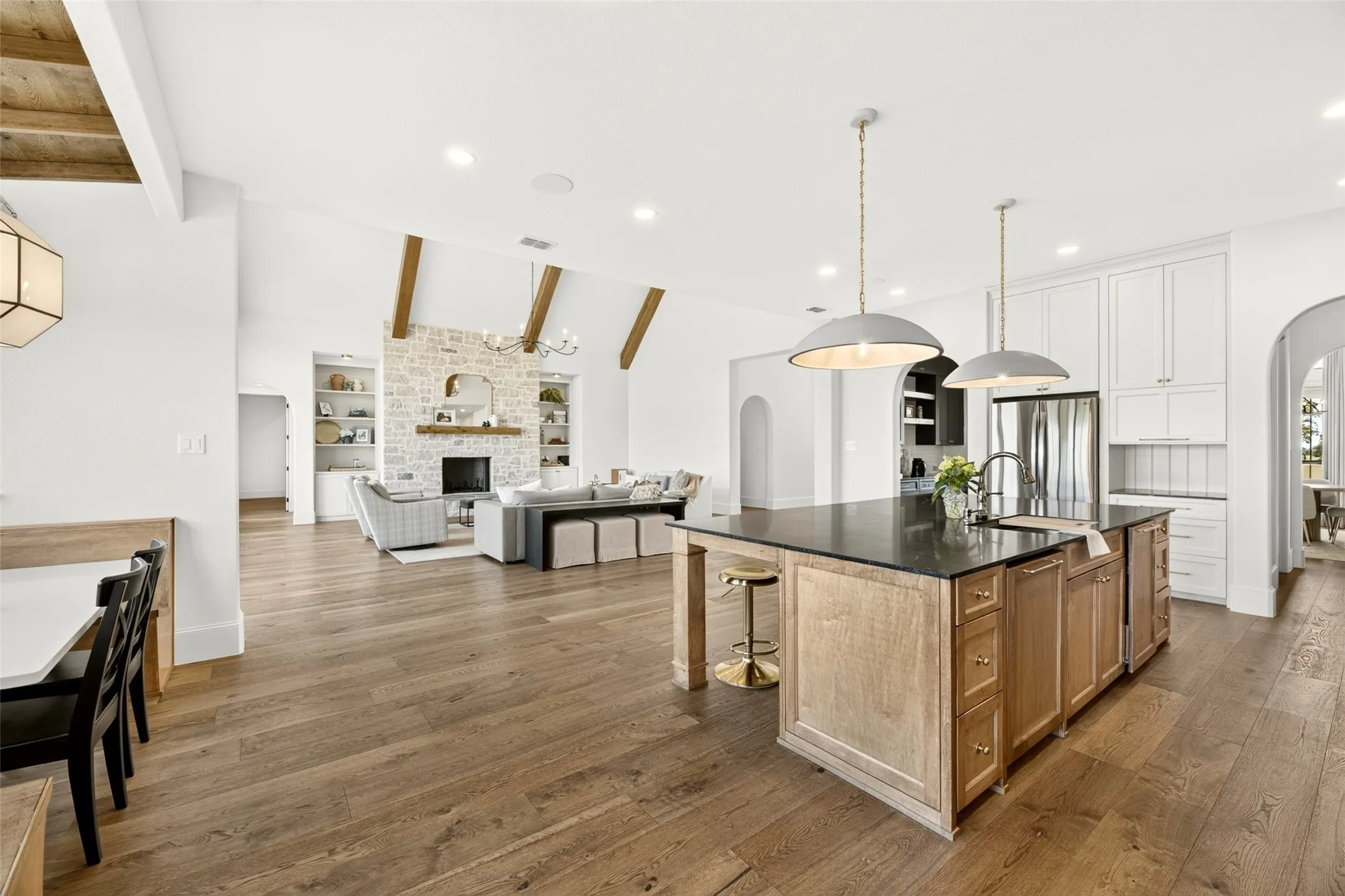 Open-concept living area with wood-finish flooring, vaulted ceilings with wood beams, and a stone-clad fireplace