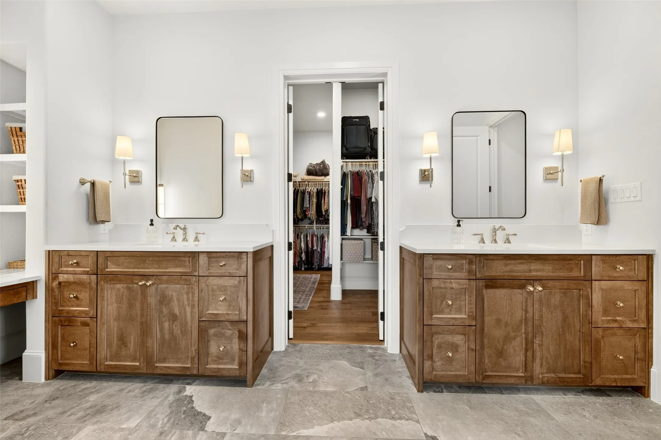 Dual vanity setup featuring wood cabinetry with gold hardware, white countertops, and wall-mounted sconces