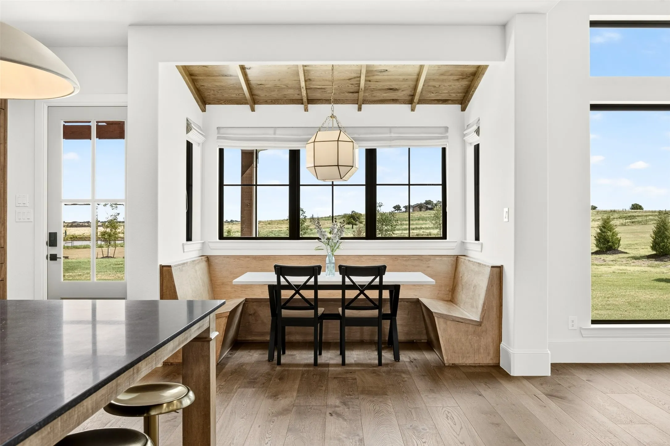Built-in wood-finish banquet seating with a hanging geometric pendant light, complemented by wood-finish flooring and expansive windows