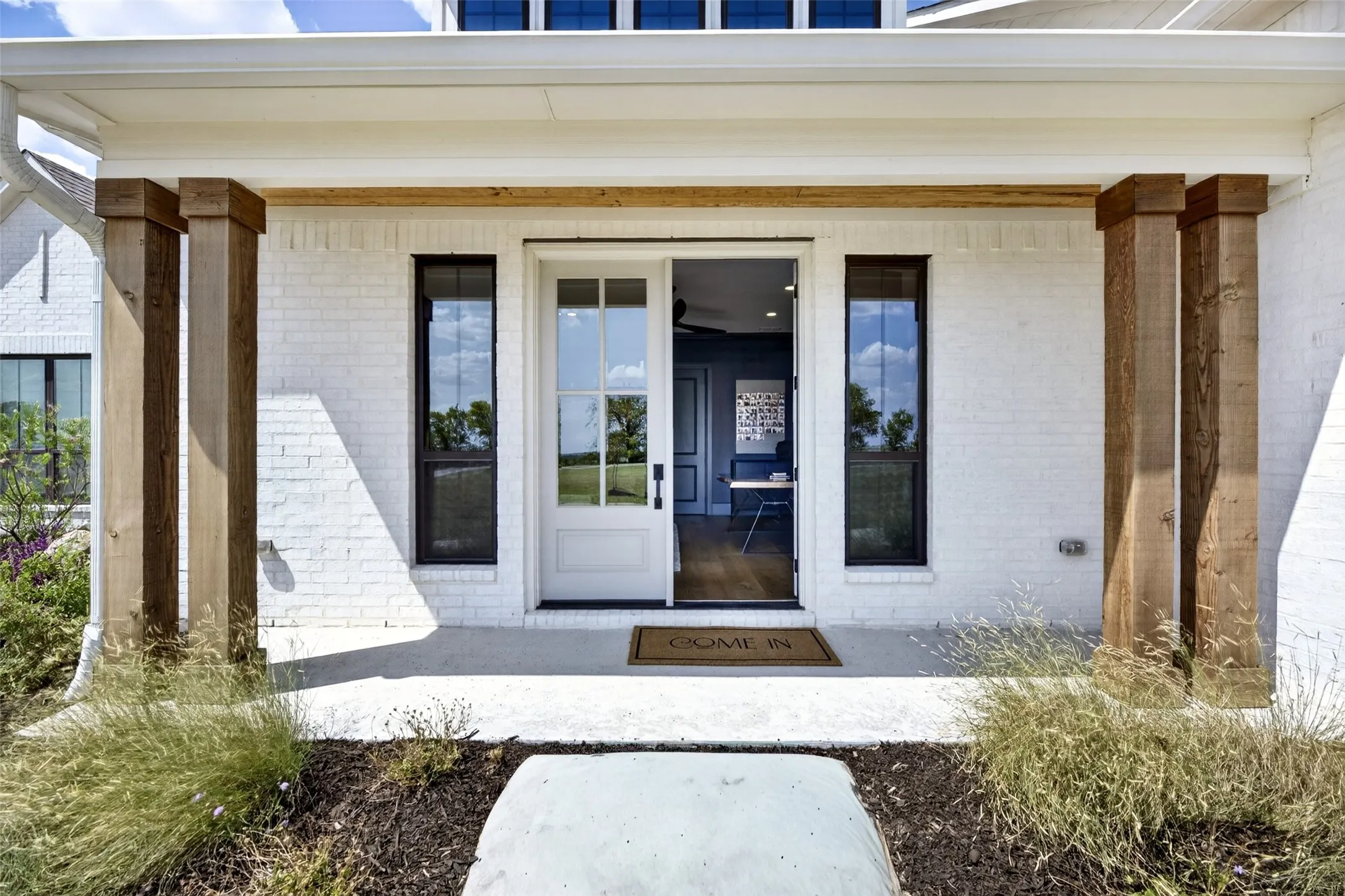 White brick exterior featuring wood columns, a covered porch, and a white paneled door with glass inserts
