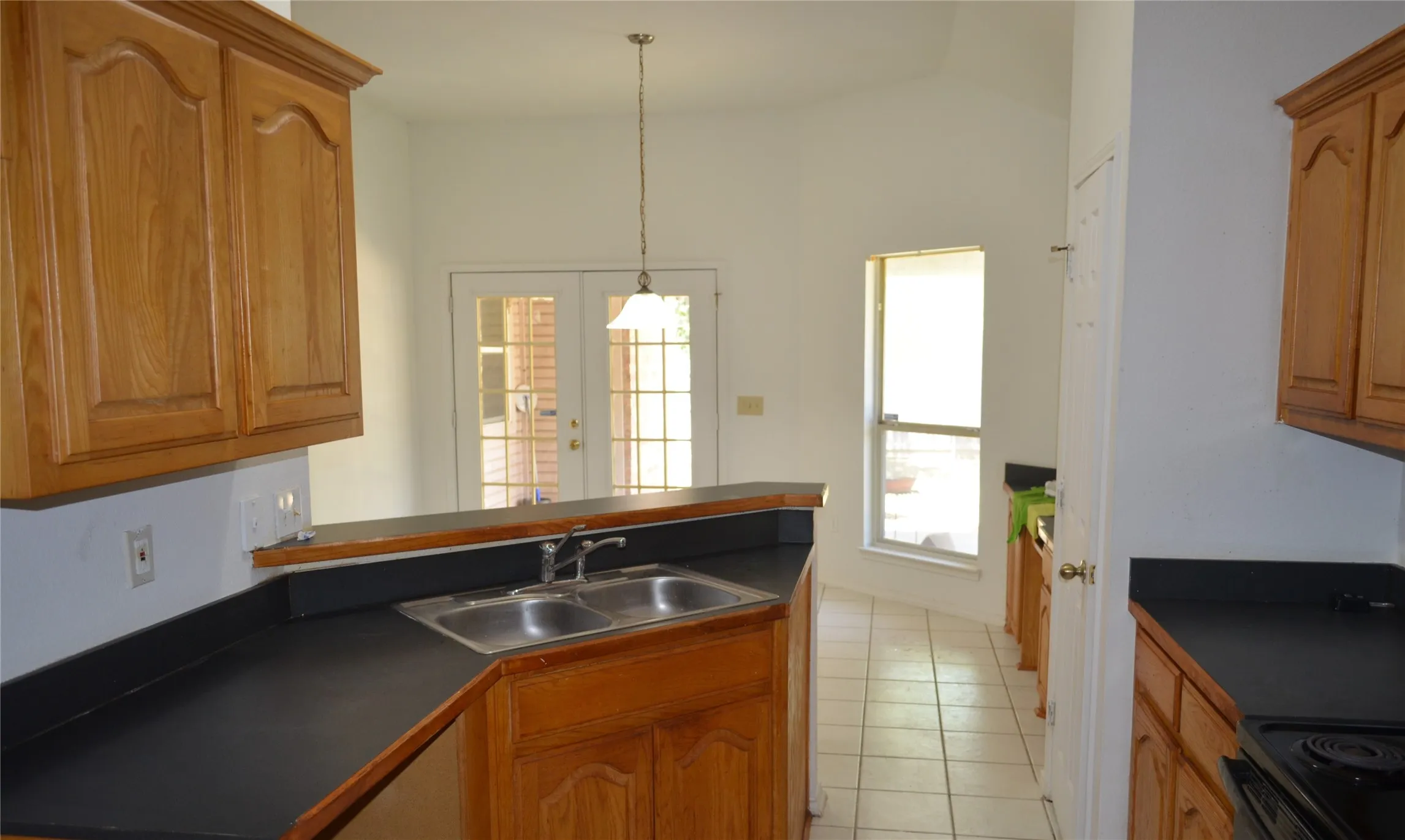 Kitchen featuring wood-finish cabinetry, black countertops, a double basin stainless steel sink, and tile flooring