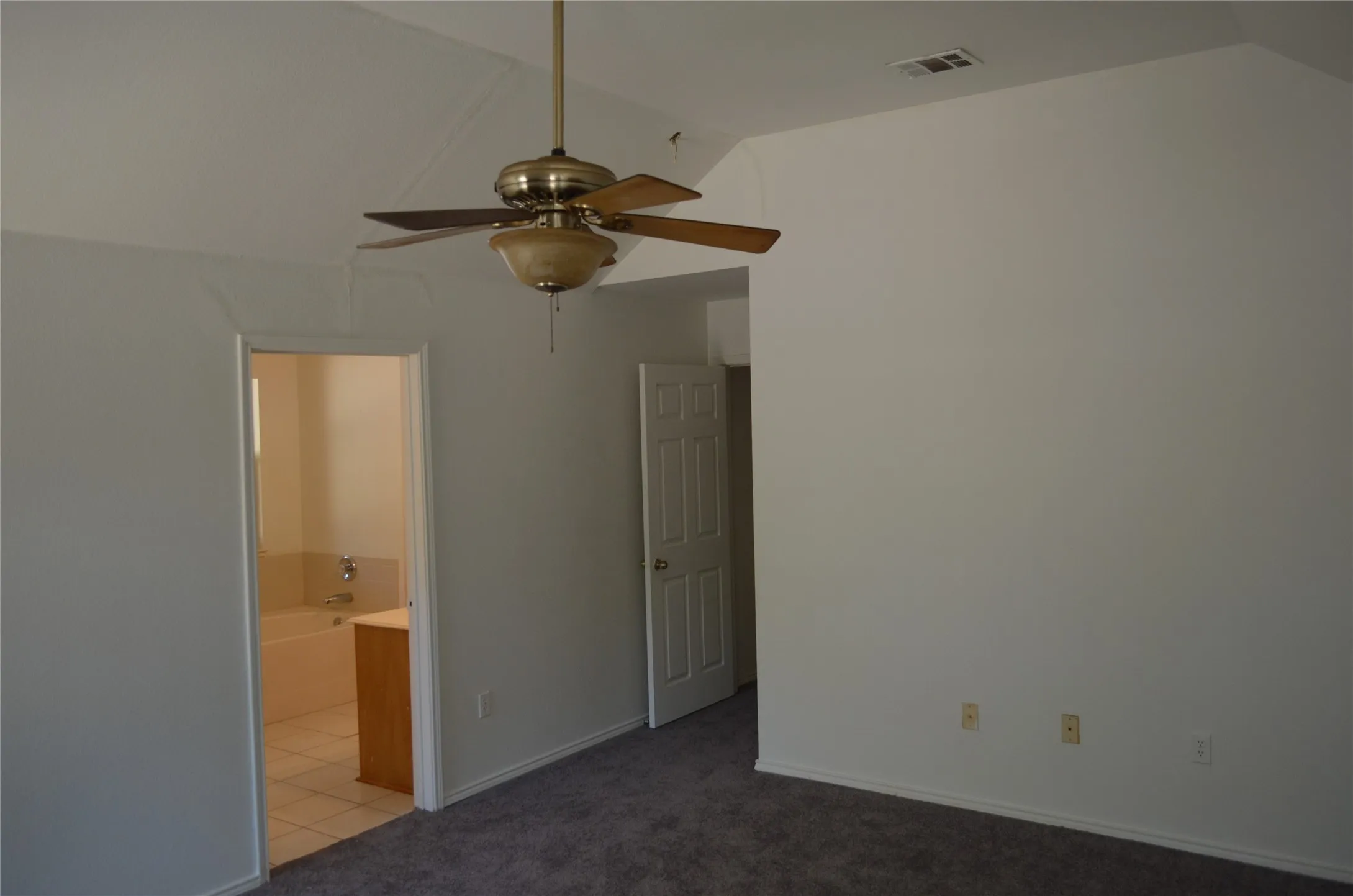 Vaulted ceiling featuring a ceiling fan with integrated lighting, carpeted flooring, and a paneled interior door