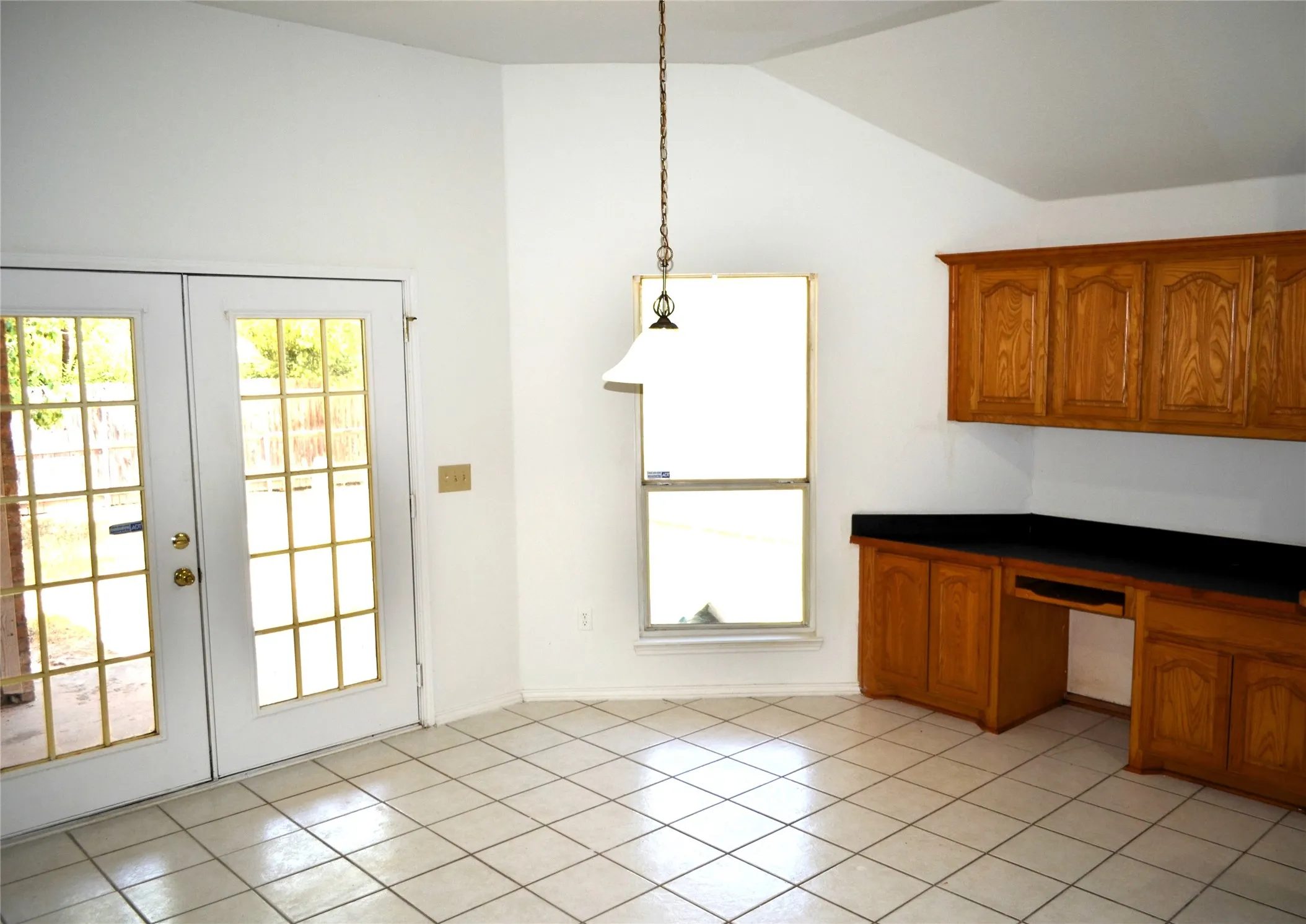 White tile flooring, vaulted ceiling, built-in wooden cabinetry, black countertops, and pendant lighting