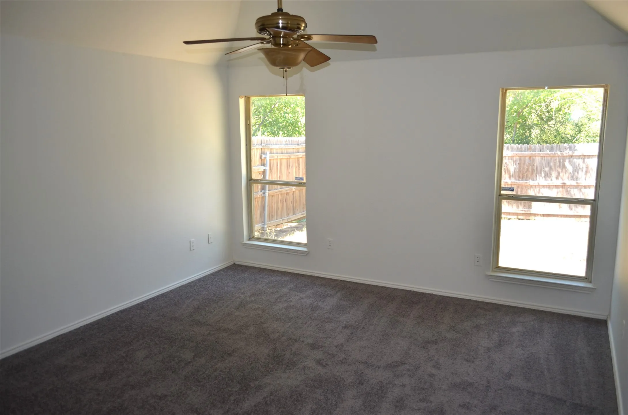 Vaulted ceiling with a ceiling fan, two windows, wall-to-wall carpeting, and white baseboards