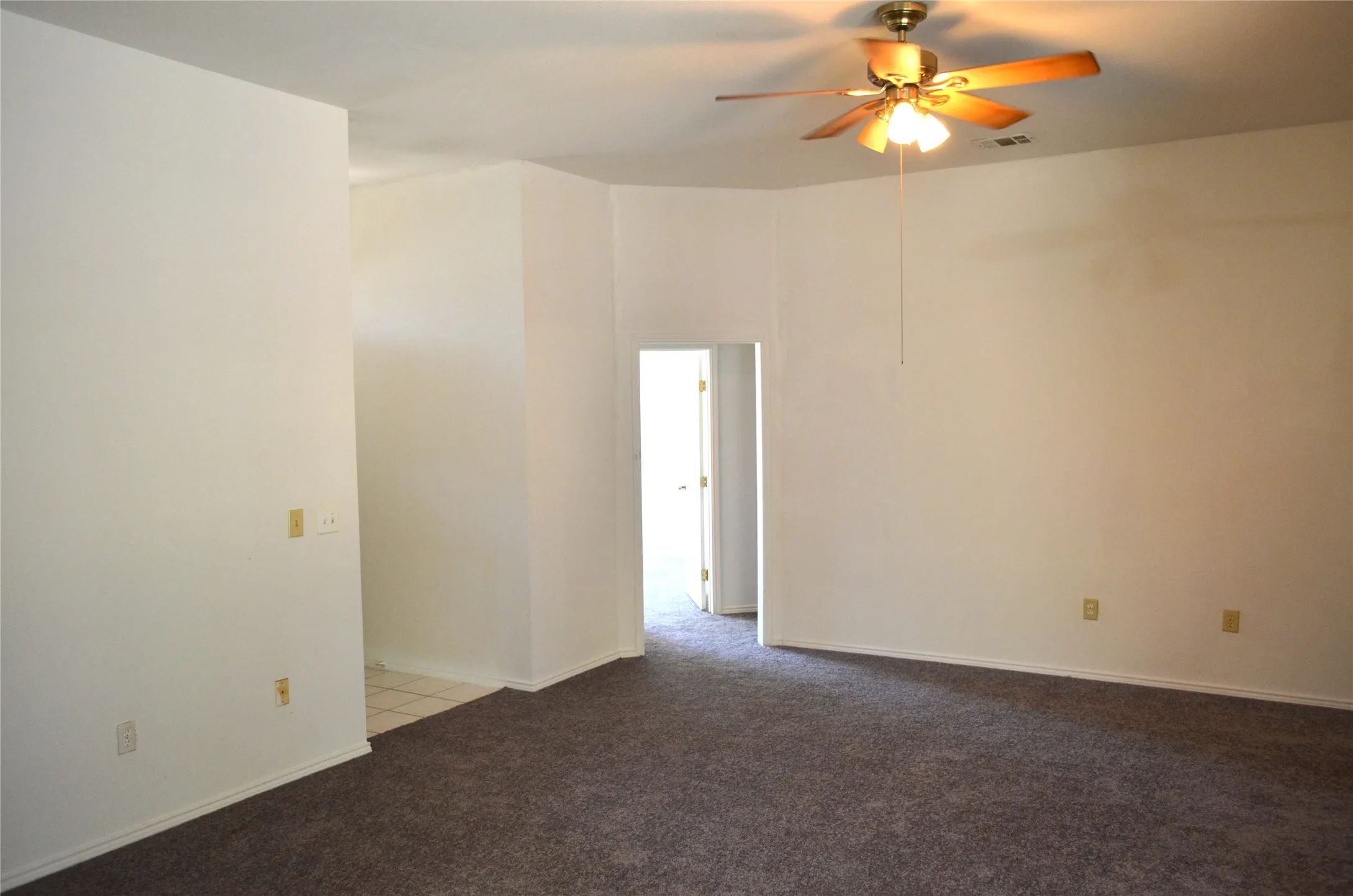 Recessed ceiling with a brass-finish ceiling fan, carpet flooring, light-toned wall paint, and a doorway with a white door