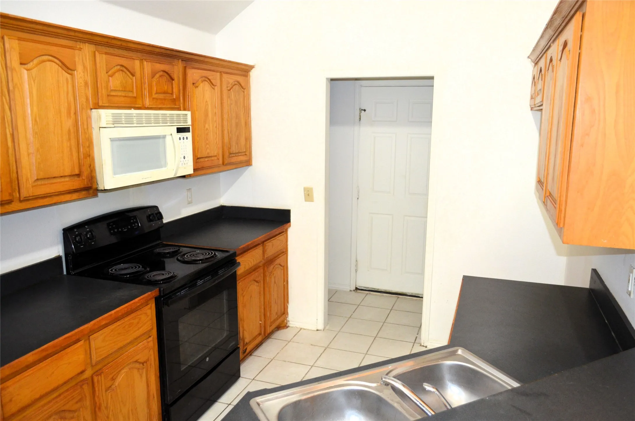 Kitchen featuring wood-finish cabinetry, black countertops, a dual basin stainless steel sink, and a black range with an overhead microwave