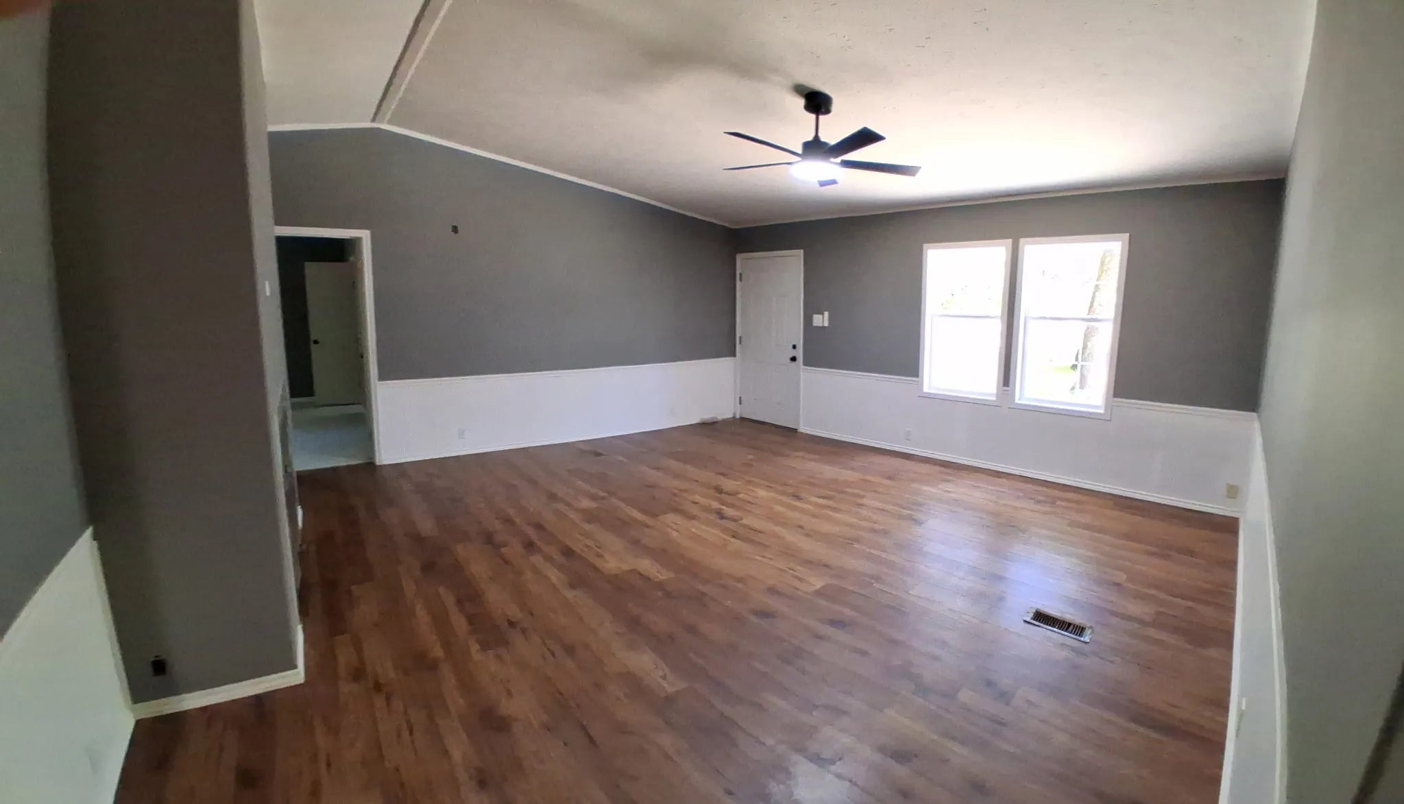 Spacious room featuring wood-finish flooring, two large windows, a ceiling fan, and two-tone wall finishes