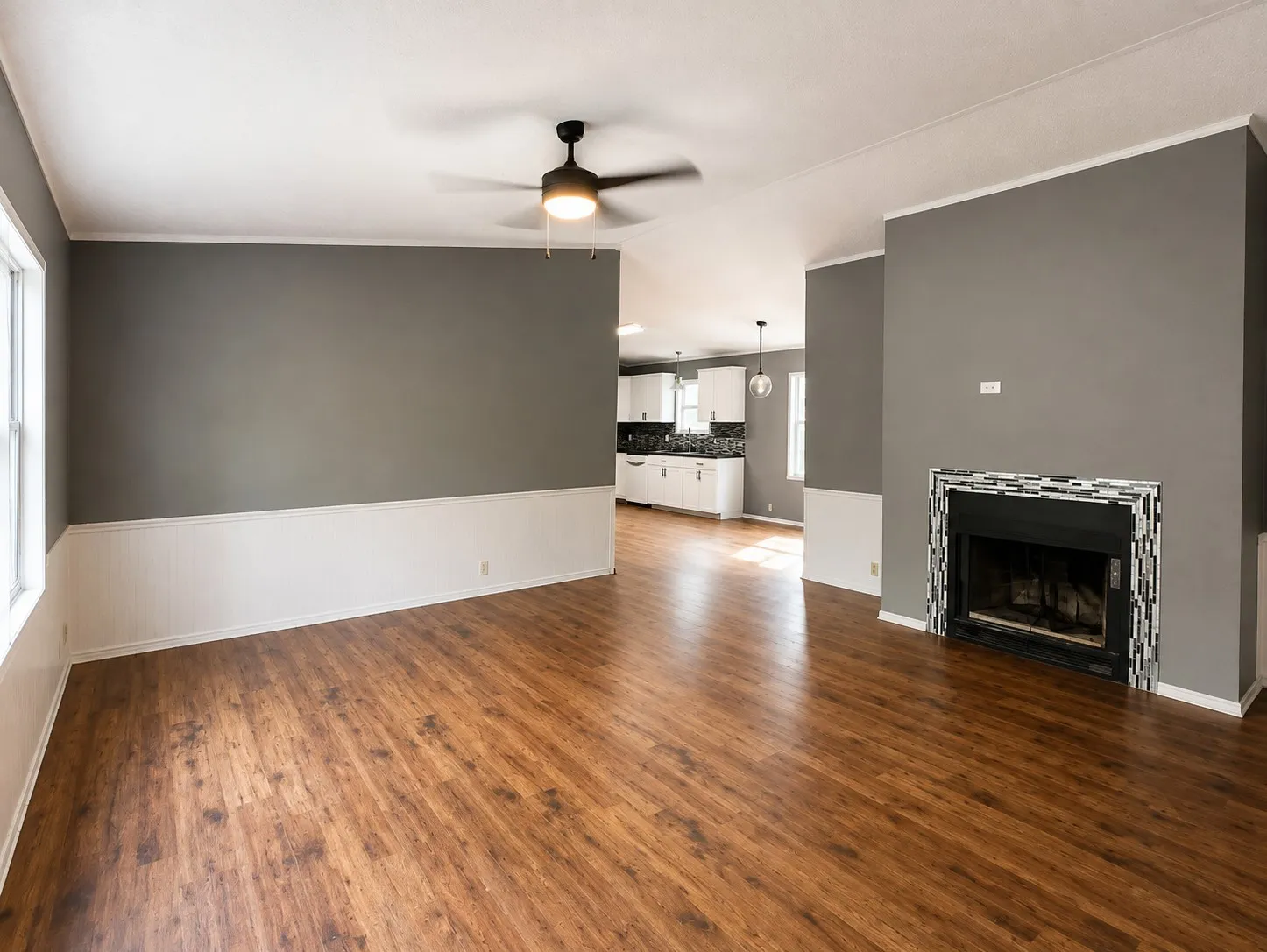 Wood-look flooring throughout, two-tone wall treatment, ceiling fan with integrated lighting, and a fireplace with a mosaic tile surround