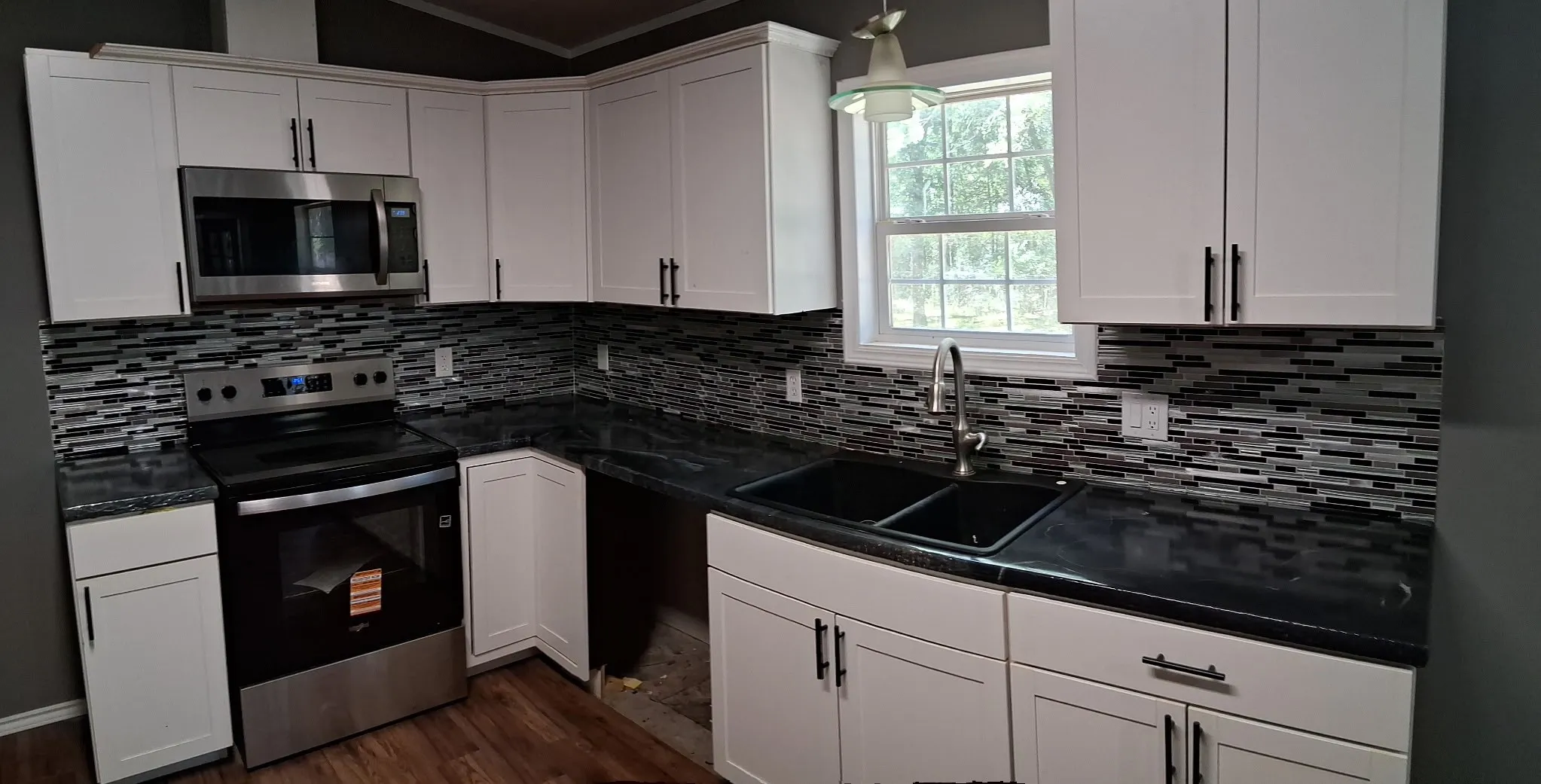 White shaker-style cabinetry with black hardware, dark countertops, tile backsplash, and stainless steel appliances