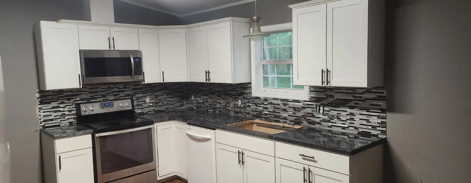 White shaker cabinetry with dark hardware, stainless steel appliances, black countertops, and a mosaic tile backsplash