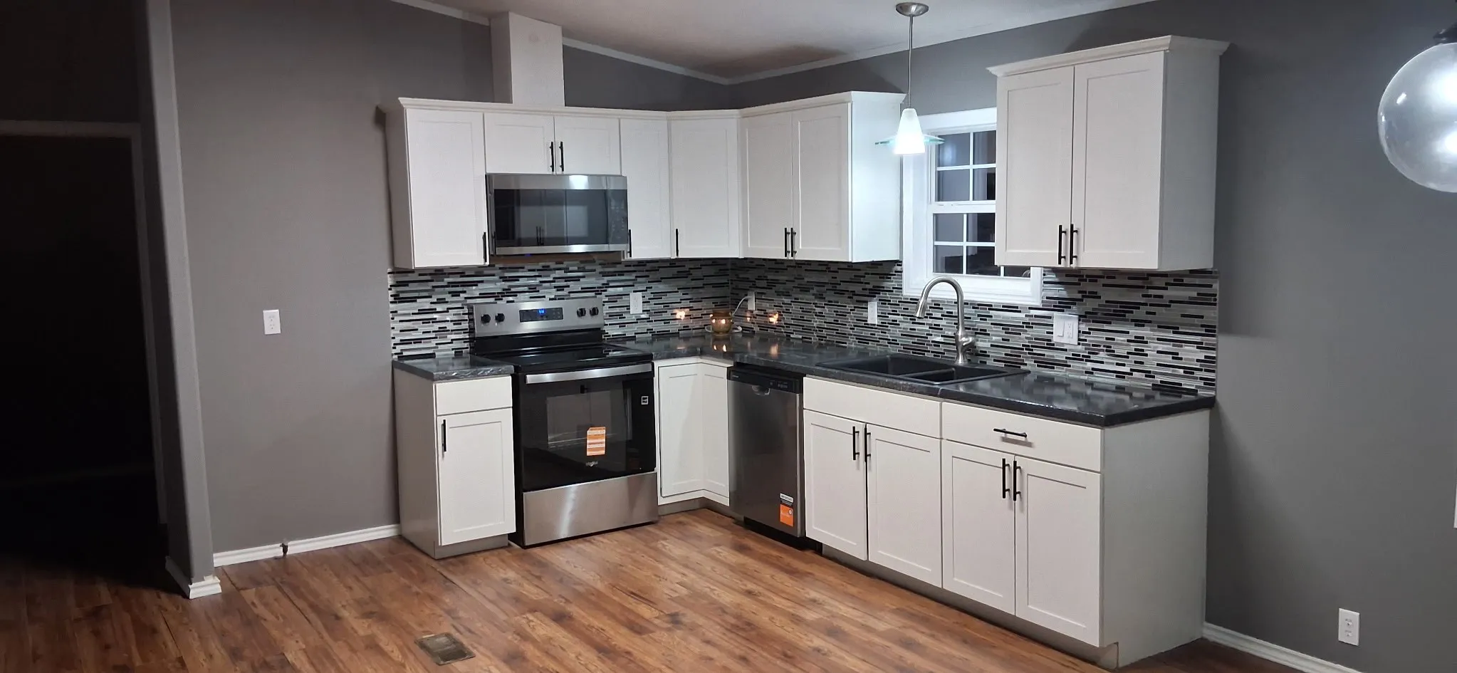 Modern kitchen featuring stainless steel appliances, white cabinetry with dark hardware, dark countertops, a mosaic tile backsplash, and wood-finish flooring